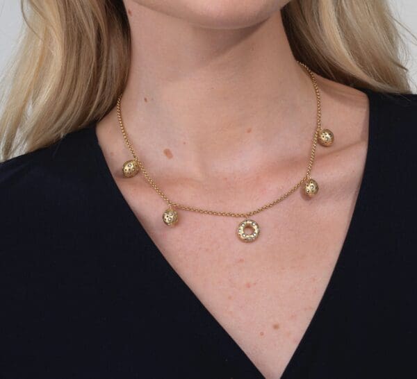 A woman wearing a necklace with five gold balls.